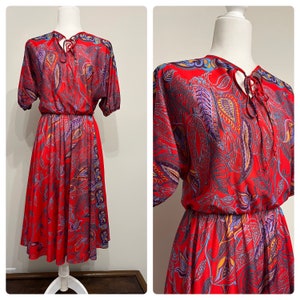 May include: A red vintage dress with a paisley print and a tie at the neck. The dress has a fitted bodice and a flowing skirt.