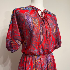 May include: A red, blue, and yellow paisley print dress with a tie at the neck and a gathered waist.