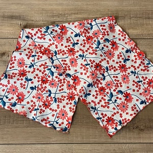 May include: A white fabric scarf with a red and blue floral pattern. The scarf has a scalloped edge and is made of a lightweight material.