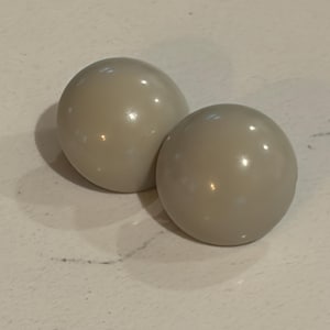 May include: Two smooth, semi-spherical buttons in a solid light gray color. Each button features a glossy, reflective surface with a rounded, dome-like shape. The buttons are positioned side-by-side, showcasing their uniform circular design.