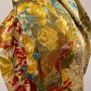 Puede incluir: Primer plano de una tela dorada con un estampado floral. El diseño presenta grandes flores amarillas y rojas con detalles verdes y azules. La tela tiene un aspecto texturizado y los pliegues crean sombras.