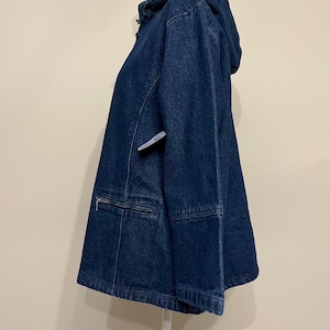 May include: A dark blue denim jacket with a hood, zipper pocket, and a drawstring hem. The jacket is displayed on a white mannequin. The jacket has a classic, casual style.