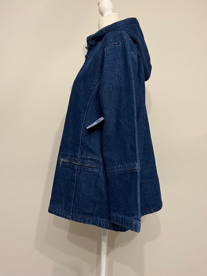 May include: A dark blue denim jacket with a hood, zipper pocket, and a drawstring hem. The jacket is displayed on a white mannequin. The jacket has a classic, casual style.