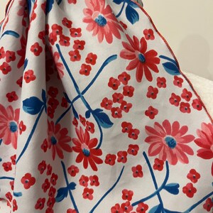 May include: A white fabric scarf with a red and blue floral pattern. The scarf has a scalloped edge.