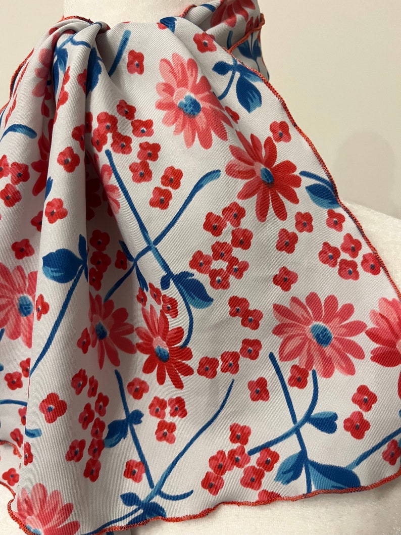 May include: A white fabric scarf with a red and blue floral pattern. The scarf has a scalloped edge.