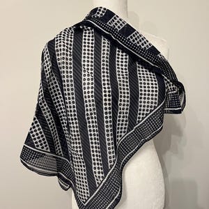 May include: A black and white patterned scarf draped over a mannequin. The scarf features a combination of vertical stripes and polka dots. The edges are bordered with a dotted pattern. The scarf is made of a lightweight, sheer fabric.