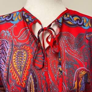 May include: Red silk blouse with a paisley print and a tie at the neck.