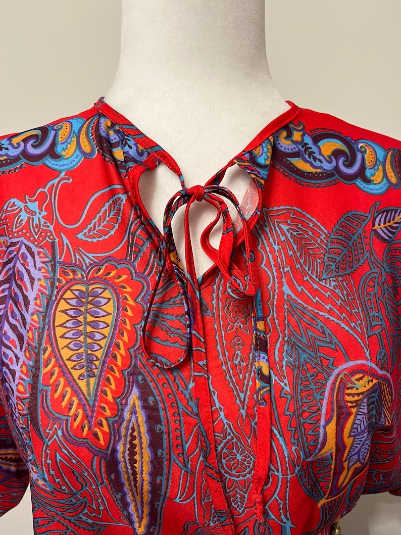 May include: Red silk blouse with a paisley print and a tie at the neck.