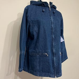 May include: A dark blue denim jacket with a hood, zipper closure, and front pockets. The jacket is displayed on a mannequin. The jacket has a classic design and is suitable for casual wear.
