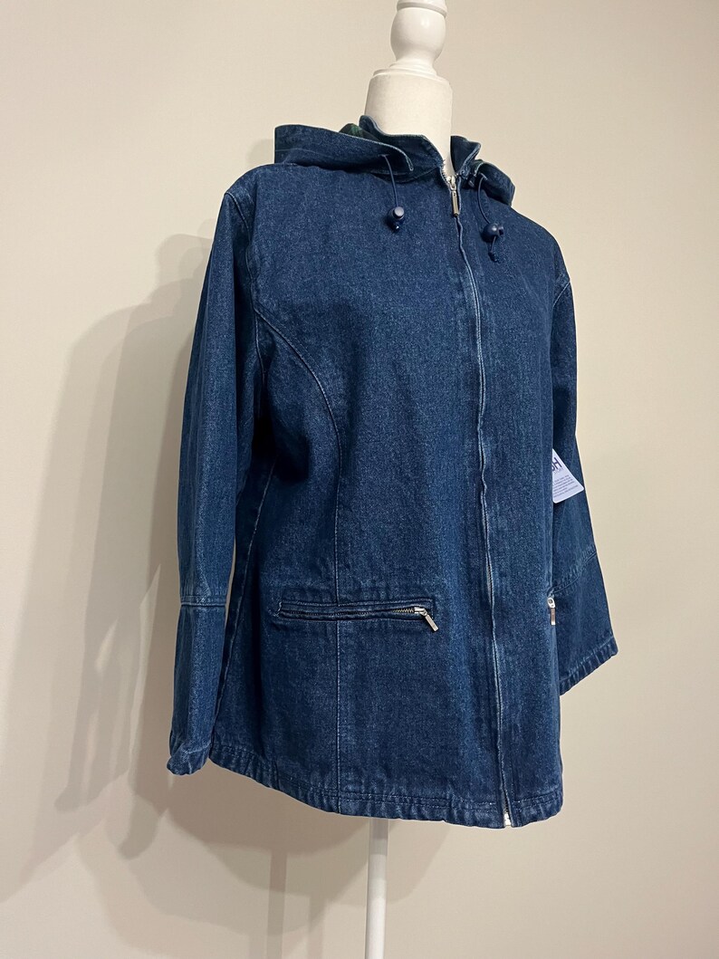 May include: A dark blue denim jacket with a hood, zipper closure, and front pockets. The jacket is displayed on a mannequin. The jacket has a classic design and is suitable for casual wear.