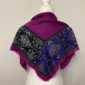 May include: A purple, blue, black, and white patterned square scarf with a fringed edge. The scarf is displayed on a white mannequin.