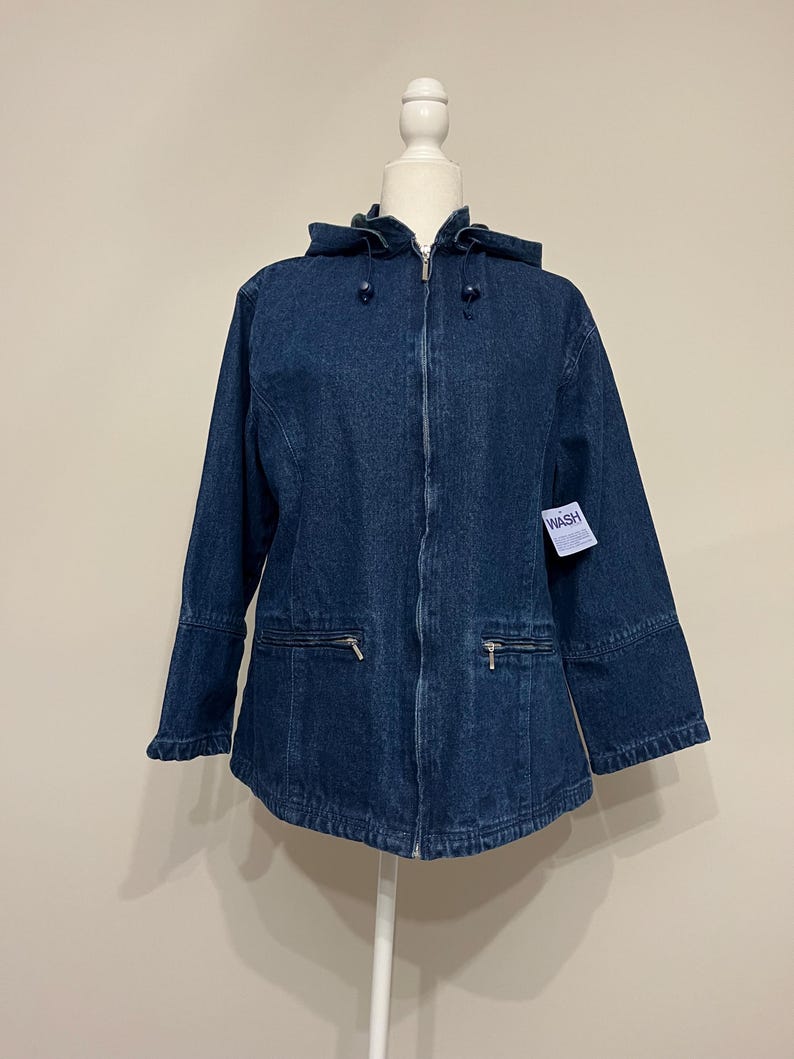 May include: A dark blue denim jacket with a hood, zipper closure, and two front pockets. The jacket is displayed on a white mannequin. The tag on the jacket reads "WASH".
