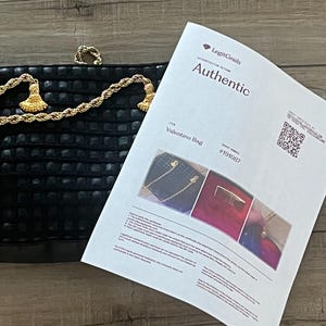 May include: A black textured handbag with a gold-tone rope chain strap and tassel accents, accompanied by a LegitGrails authentication certificate labeled Authentic for a Valentino Bag with order number 191087 and a QR code for verification.