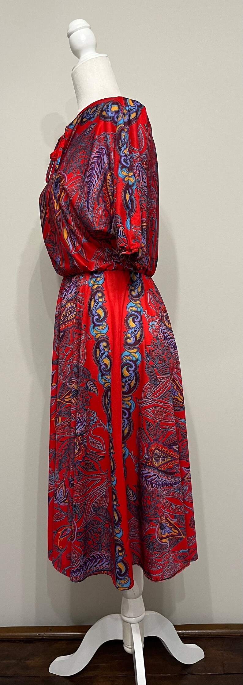 May include: A red dress with a floral print. The dress has a gathered neckline and short sleeves. The dress is on a white mannequin.