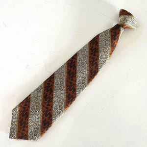 May include: A clip-on necktie featuring alternating diagonal stripes of metallic silver with a light gray intricate scrollwork pattern and deep copper brown with a dark brown repeating silhouette pattern of a small animal or creature.