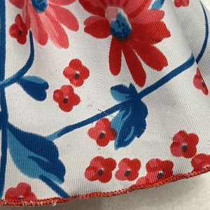 May include: A white fabric with a red and blue floral pattern. The fabric has a red trim around the edge.