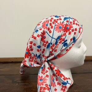 May include: A white headscarf with a red and blue floral pattern. The scarf is tied around a white mannequin head.