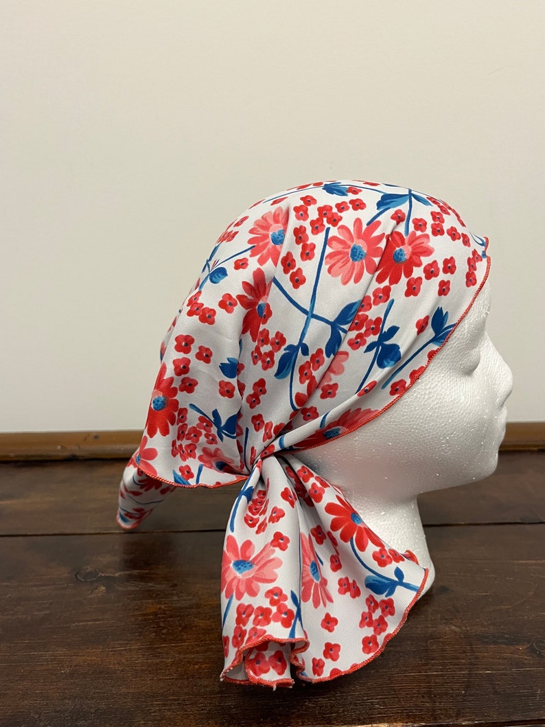 May include: A white headscarf with a red and blue floral pattern. The scarf is tied around a white mannequin head.