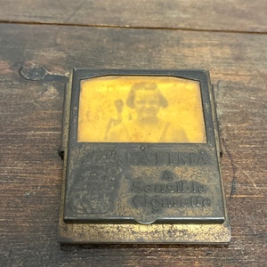May include: Vintage brass cigarette case with a portrait and the text "FATIMA A Sensible Cigarette." The case has a rectangular shape with a hinged lid and a clasp. The brass has a worn, aged appearance.