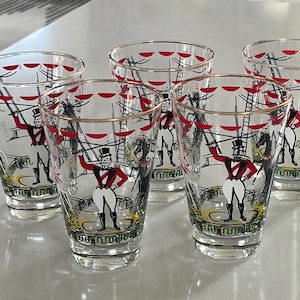 May include: Set of six vintage clear glass tumblers with gold rims. Each tumbler features a circus performer in a red jacket and white pants. The design includes a circus tent and ladder in black and red.