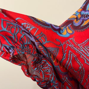 May include: Red fabric with a blue, purple, and yellow paisley pattern. The fabric has a gathered edge.