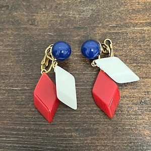 May include: A pair of clip-on earrings with red, white, and blue geometric shapes. The earrings feature a blue round bead at the top, followed by a white diamond shape, and a red diamond shape.