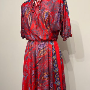May include: A red maxi dress with a paisley print and a tie at the neck.