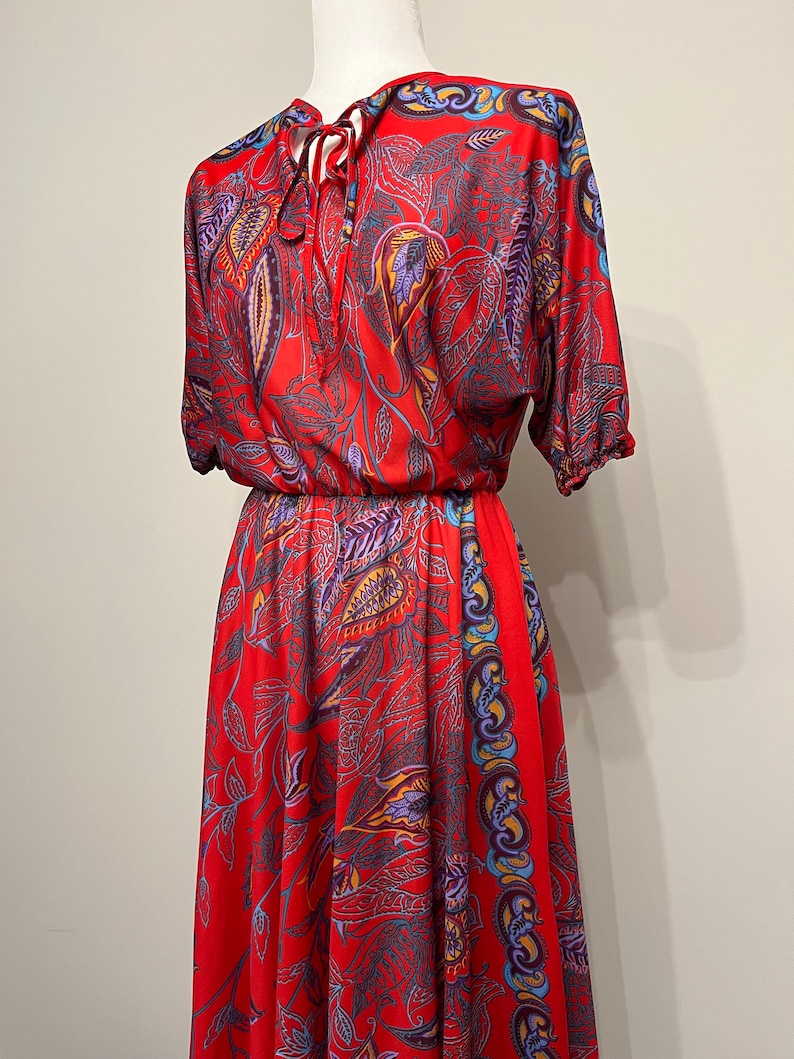 May include: A red maxi dress with a paisley print and a tie at the neck.