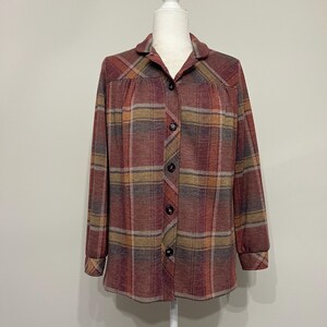 May include: A button-down plaid shirt in shades of burgundy, brown, and gold. The long-sleeved shirt features a classic collar and buttoned cuffs. The shirt is displayed on a white mannequin.