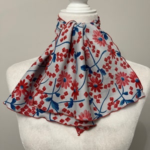 May include: A white scarf with a red and blue floral pattern. The scarf is tied around a white mannequin's neck.