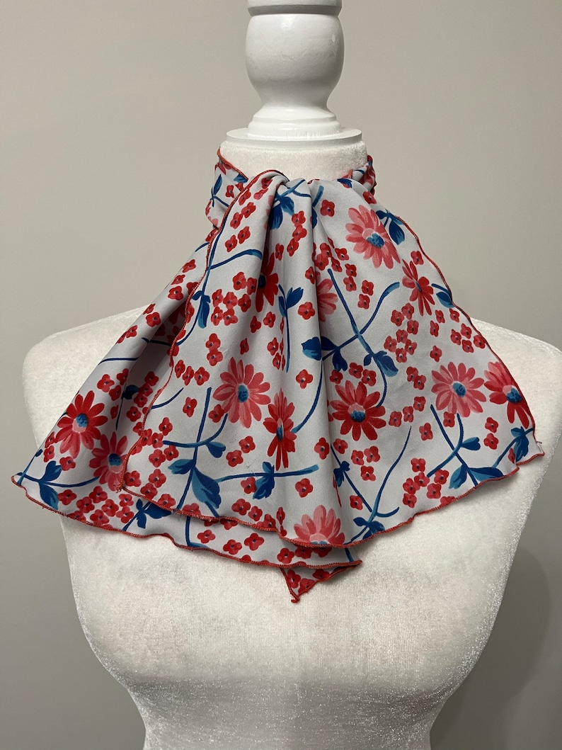 May include: A white scarf with a red and blue floral pattern. The scarf is tied around a white mannequin's neck.