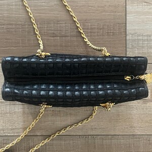 May include: A black rectangular handbag with a textured grid pattern and a top zipper closure. The bag features a gold-tone metal chain strap and a decorative gold-tone metal fan-shaped zipper pull attached to the zipper slider.