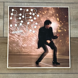 May include: A vintage vinyl record album cover featuring the text "PETER WOLF" in a white, stylized font with a dotted design. The album title "LIGHTS OUT" is also visible. The cover art depicts a man in a black suit.