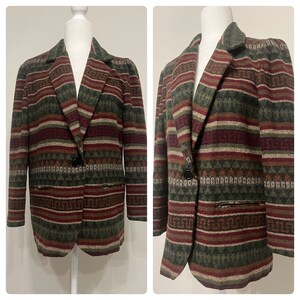 Puede incluir: Blazer estampado en tonos verdes, burdeos y beige. La chaqueta presenta un cierre de un solo botón, solapas con muescas y dos bolsillos delanteros. La tela tiene un aspecto texturizado con rayas horizontales y patrones geométricos.