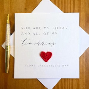 May include: A white Valentine's Day card with the text "YOU ARE MY TODAY, AND ALL OF MY TOMORROWS" and a small red crocheted heart. A gold and crystal pen rests on the left side of the card. The words "HAPPY VALENTINE'S DAY" are printed at the bottom.