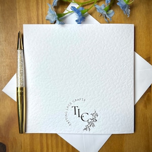 May include: A white card with a black circle logo that says "Tatting Lace Crafts" and the initials "TLC" in the center. The logo is surrounded by a small floral design.