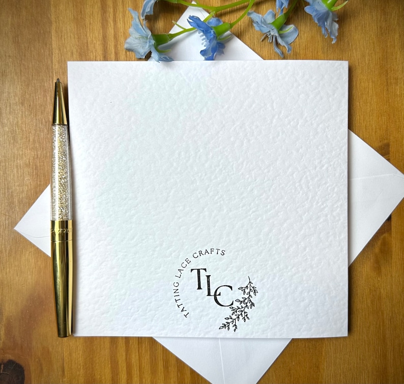 May include: A white card with a black circle logo that says "Tatting Lace Crafts" and the initials "TLC" in the center. The logo is surrounded by a small floral design.