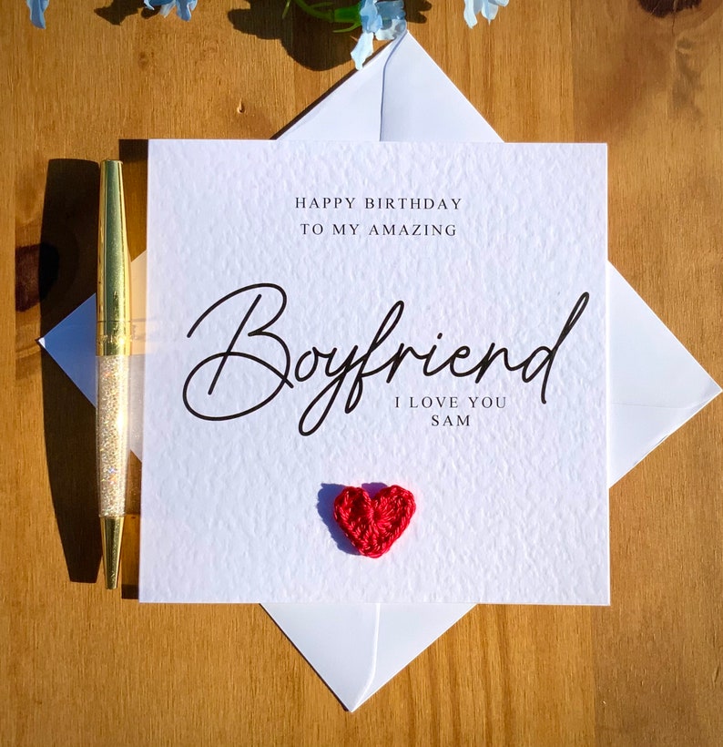 May include: White card with the text "Happy Birthday to my amazing Boyfriend I love you Sam" in black script. A small red crocheted heart is in the bottom right corner.
