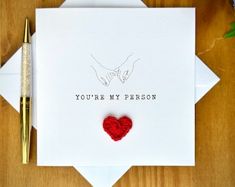 May include: A white card with a black line drawing of two hands holding pinkies, the text "YOU'RE MY PERSON" and a red crocheted heart.