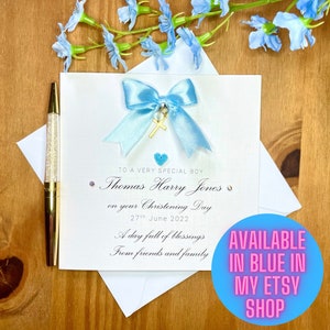 Puede incluir: Una tarjeta blanca con una cinta azul y un dije de cruz dorada. La tarjeta dice "To a very special boy Thomas Harry Jones on your Christening Day 27th June 2022 A day full of blessings From friends and family".