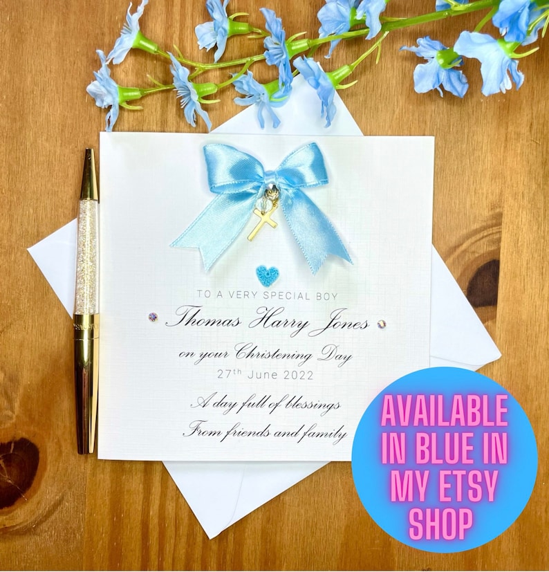 Puede incluir: Una tarjeta blanca con una cinta azul y un dije de cruz dorada. La tarjeta dice "To a very special boy Thomas Harry Jones on your Christening Day 27th June 2022 A day full of blessings From friends and family".
