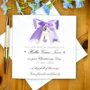 Puede incluir: Una tarjeta blanca con un lazo morado y un dije de cruz dorada. La tarjeta dice "To a very special goddaughter Hallie-Grace Teece on your Christening Day 2nd April 2023 A day full of blessings From friends and family".