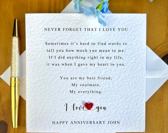 May include: A white card with a red heart and the text "NEVER FORGET THAT I LOVE YOU" and "HAPPY ANNIVERSARY JOHN". The card has a message about love and friendship.