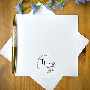 Pode incluir: Um cart&atilde;o branco com um logotipo preto e branco que diz "Tatting Lace Crafts" e "TLC" em um c&iacute;rculo com um pequeno desenho floral. Uma caneta dourada est&aacute; no lado esquerdo do cart&atilde;o.