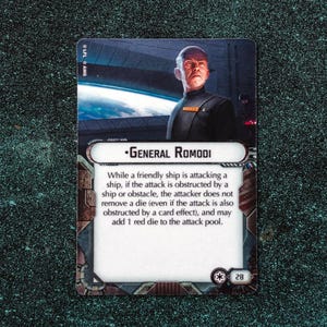 Peut inclure: Carte Star Wars avec le Général Romodi. La carte présente un portrait du personnage et du texte de jeu. La carte est principalement blanche, noire et grise, avec un fond sombre. La carte porte également le numéro 28.