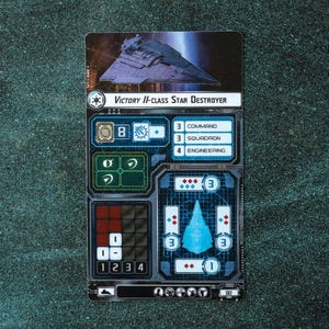 May include: A blue and gray Star Wars Victory II-class Star Destroyer card game ship card with a blue and gray ship illustration, a ship stats section, and the text "VICTORY II-CLASS STAR DESTROYER".