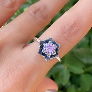 May include: A silver ring with a black flower design and a pink gemstone in the center.