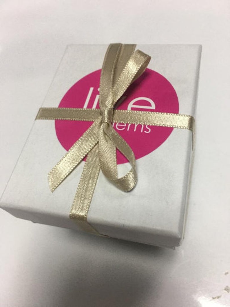Op de afbeelding: Een witte cadeaudoos met een gouden lint dat in een strik is gebonden. De doos heeft een roze cirkel met de tekst "Live Items" erop.