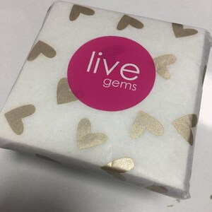 Op de afbeelding: Wit cadeaupapier met gouden harten en de tekst "live gems" in een roze cirkel.