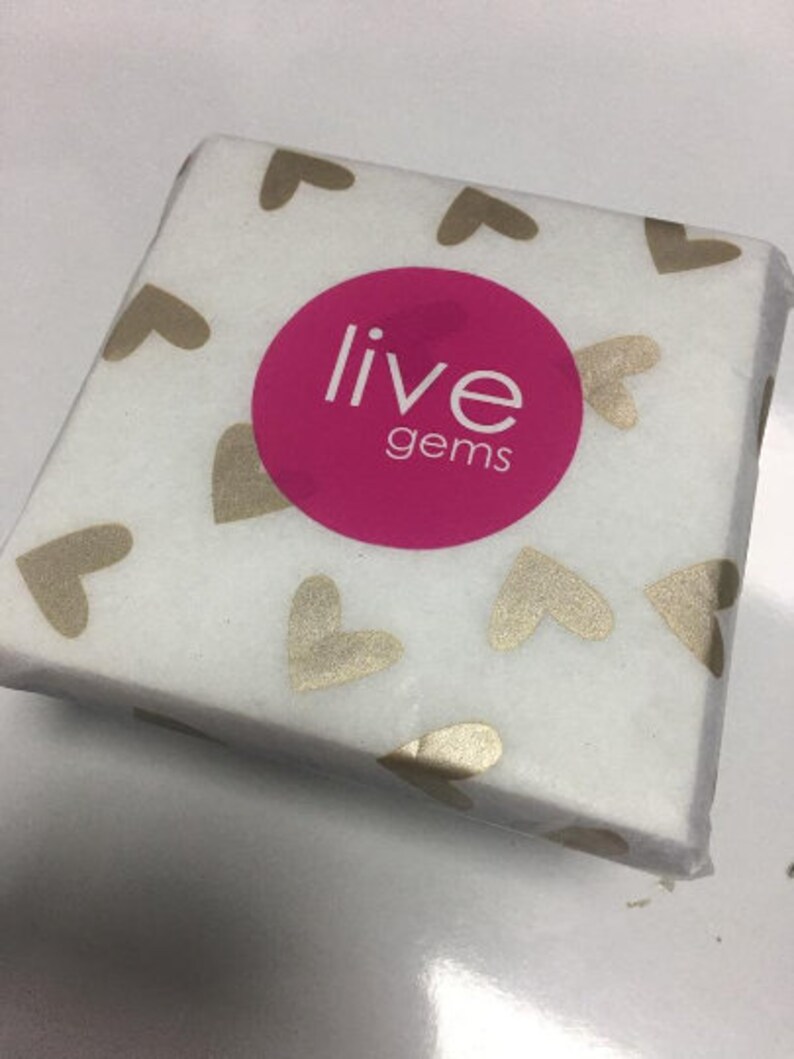 Op de afbeelding: Wit cadeaupapier met gouden harten en de tekst "live gems" in een roze cirkel.